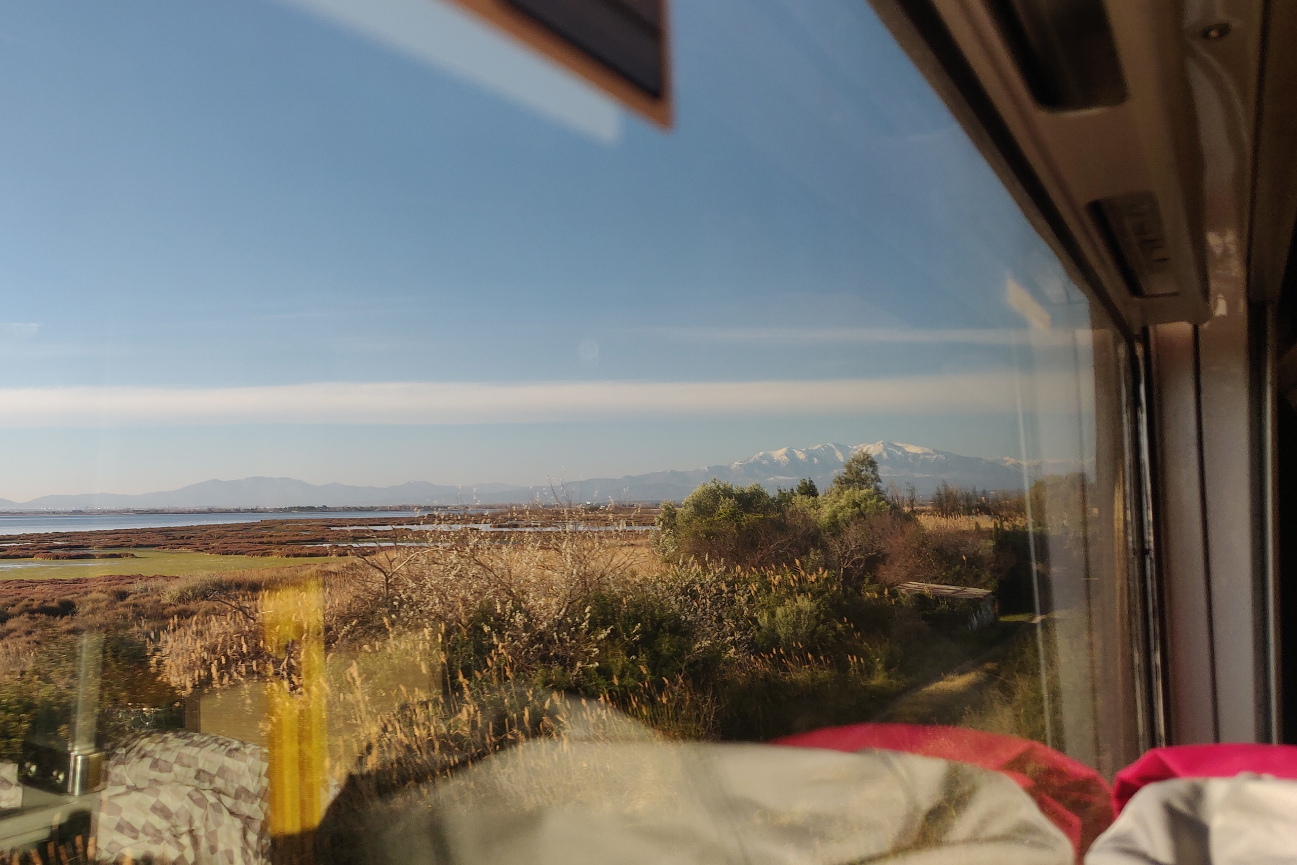 Blick aus dem Zugfenster: Die Küste Südfrankreichs mit den schneebedeckten Pyrenäen am Horizont.