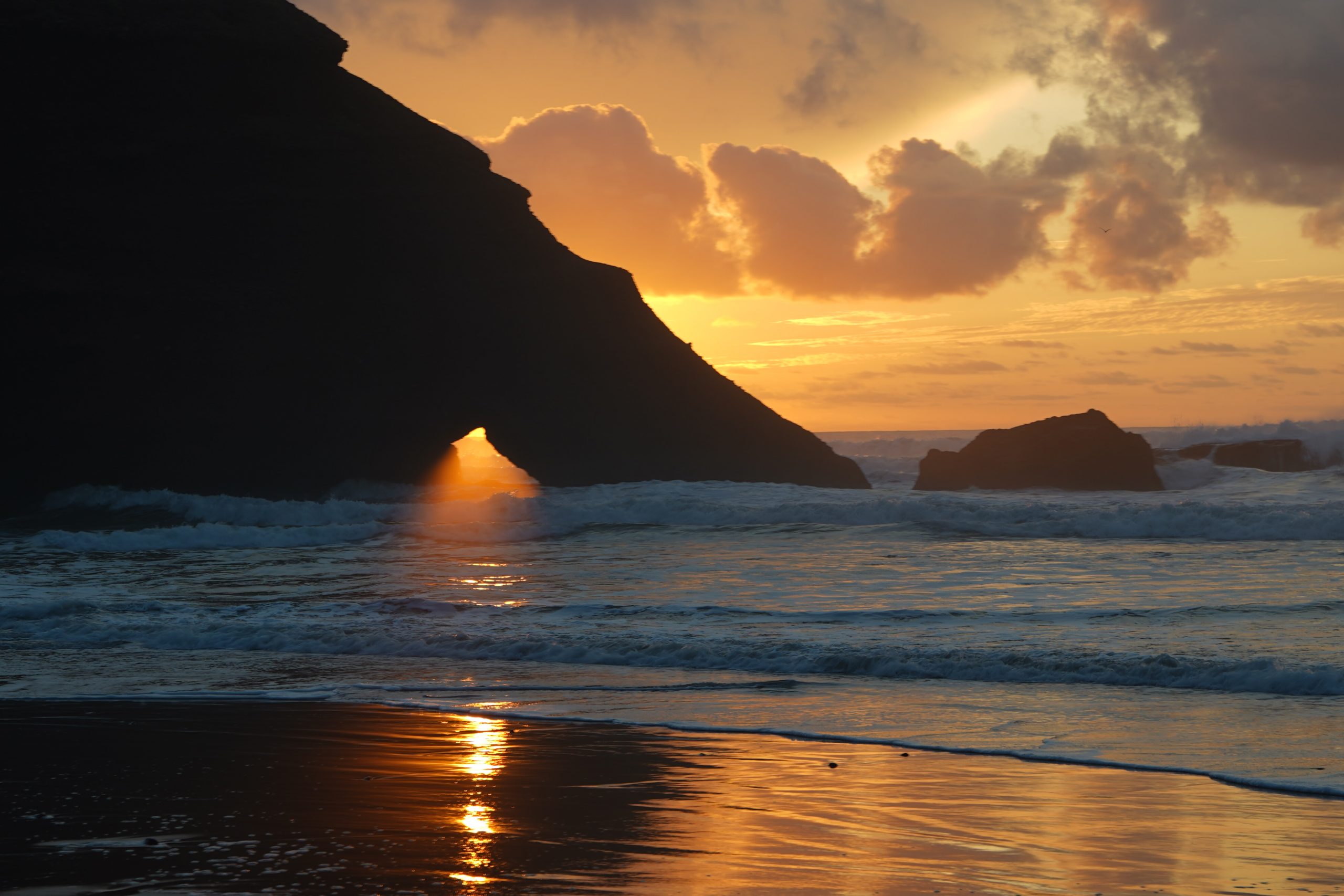 Der letzte goldene Lichtstrahl der Sonne fällt durch einen Felsspalt an einem marokkanischen Strand.