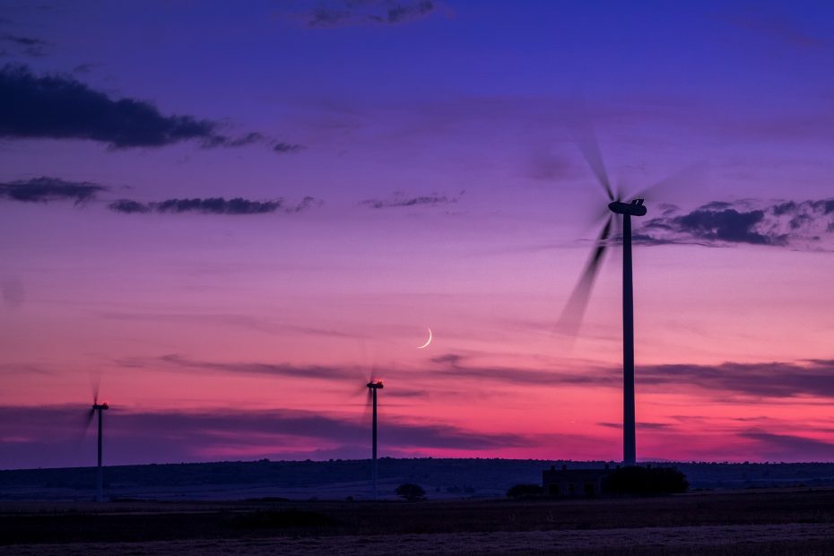 Zwei Windräder erzeugen nachhaltig Strom vor einem rosa-violetten Sonnenuntergang.