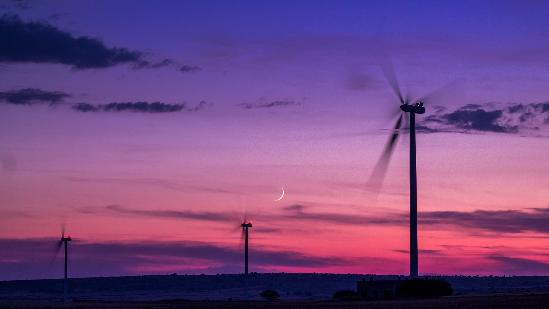 Zwei Windräder erzeugen nachhaltig Strom vor einem rosa-violetten Sonnenuntergang.