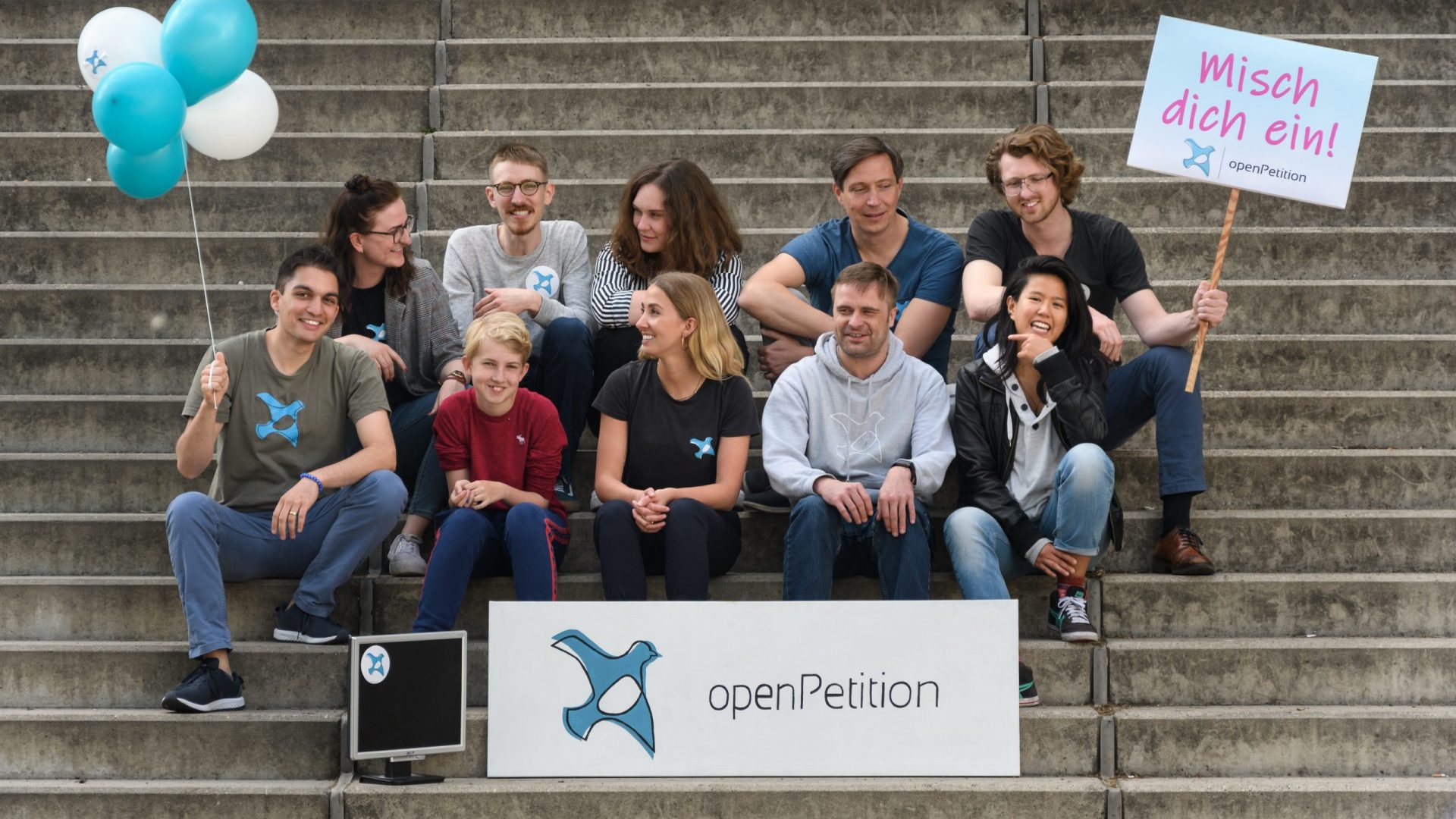 Das Team von openPetition sitzt auf einer Treppe und macht Werbung für Petitionen.